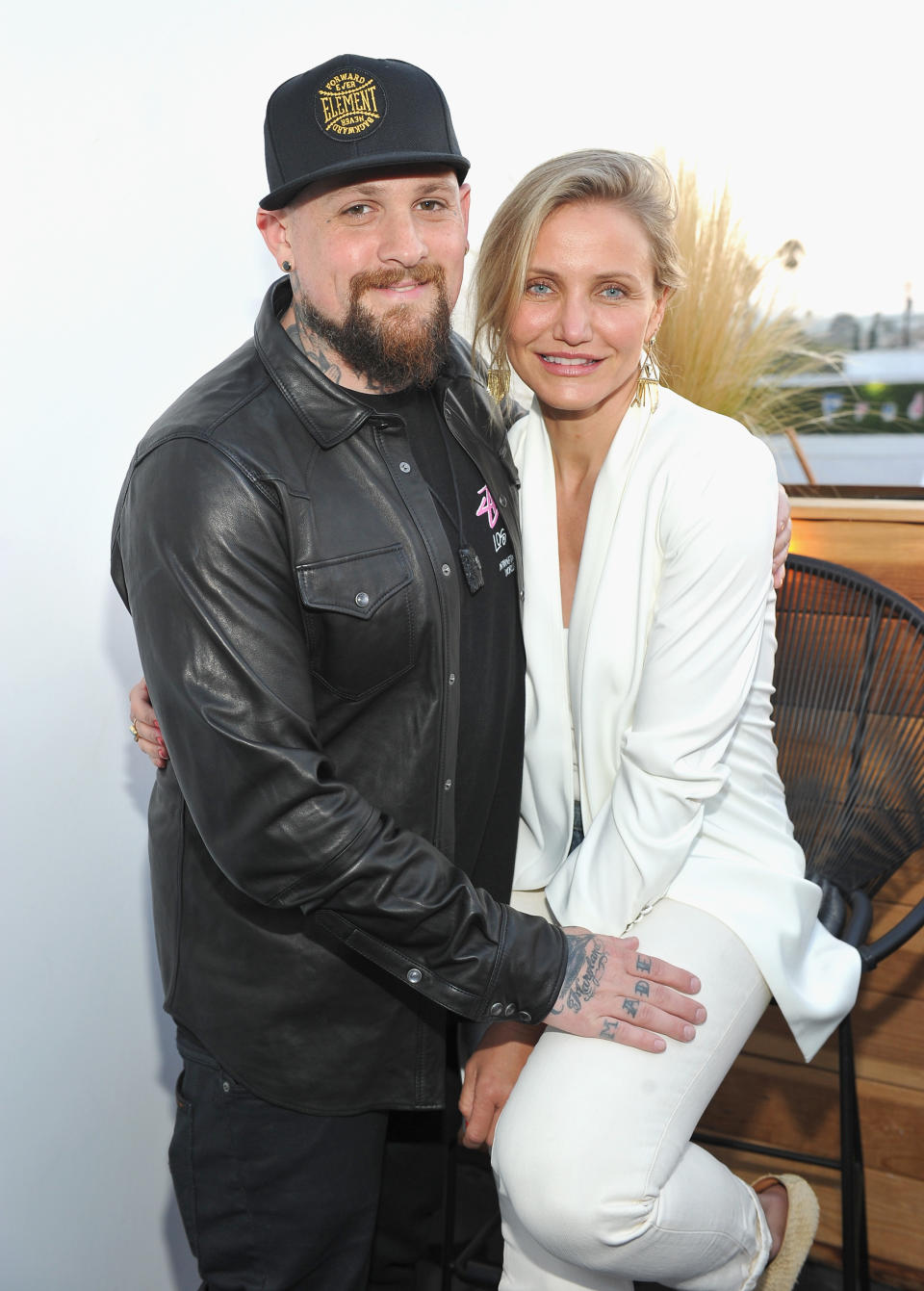 Benji in a leather jacket and cap with Cameron, in a white blazer, both smiling