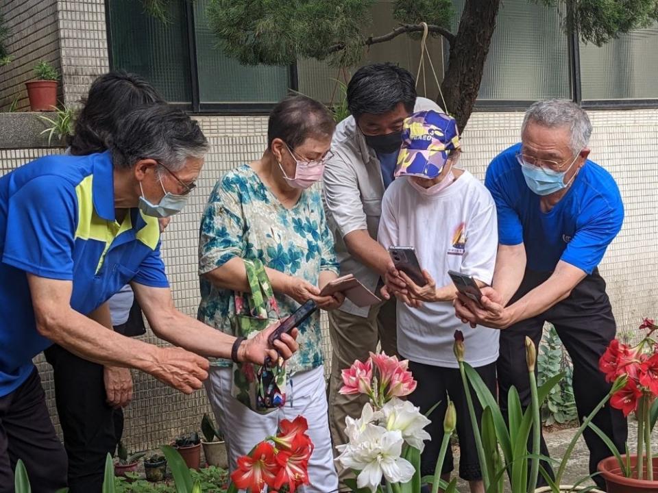 《圖說》王建博老師(右三)熱情帶領八德榮家住民長輩在花園中悉心解說手機相機功能。〈八德榮家提供〉