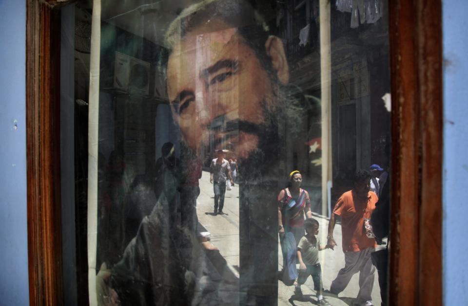 FILE - In this May 15, 2015 file photo, pedestrians are reflected in a post office window where a poster of Fidel Castro hangs in Havana, Cuba. (AP Photo/Desmond Boylan, File)