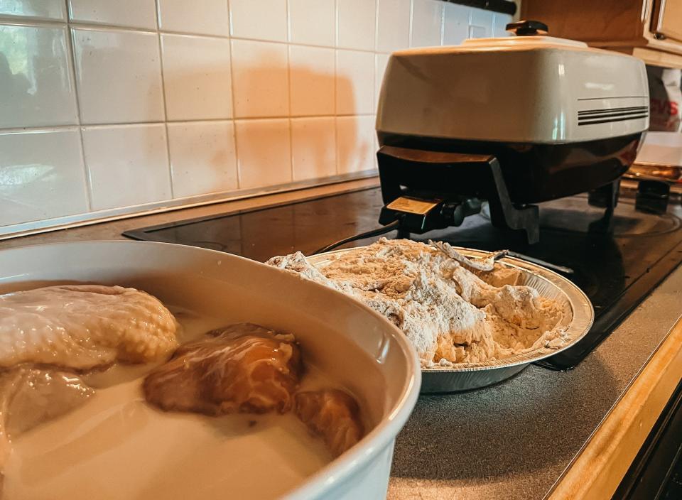 chicken in buttermilk next to a pan of flour near a deep fryer