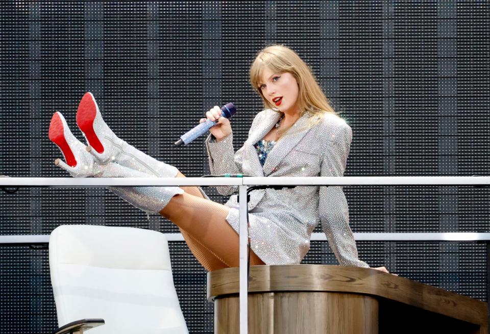 Taylor Swift sat on a desk, on stage performing during her Eras tour