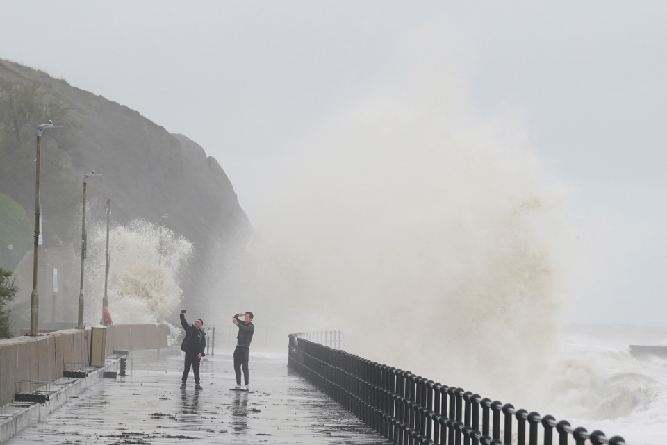 People photograph the waves crashing over the promenade in Folkestone, Kent (PA)