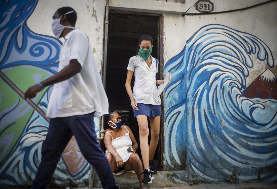 Dos trabajadores de salud provistos de mascarilas se retiran de un inmueble tras verificar que la zona esta libre de COVID-19 en La Habana, Cuba, el martes 31 de marzo de 2020. (AP Foto/Ramón Espinosa)