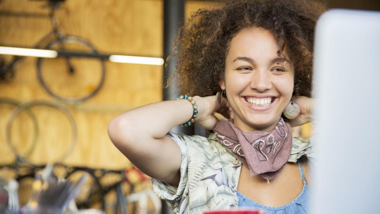 smiling woman at laptop in bike shop adjusting neck scarf