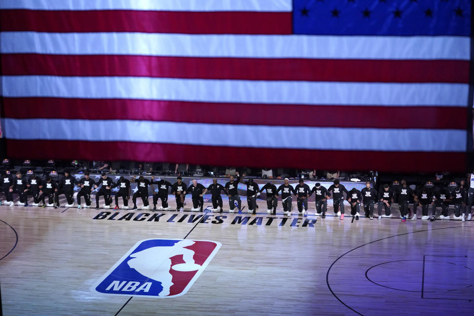 Members of the Orlando Magic and Brooklyn Nets kneel around a Black Lives Matter logo during the national anthem before the start of an NBA basketball game Friday, July 31, 2020, in Lake Buena Vista, Fla. (AP Photo/Ashley Landis, Pool)