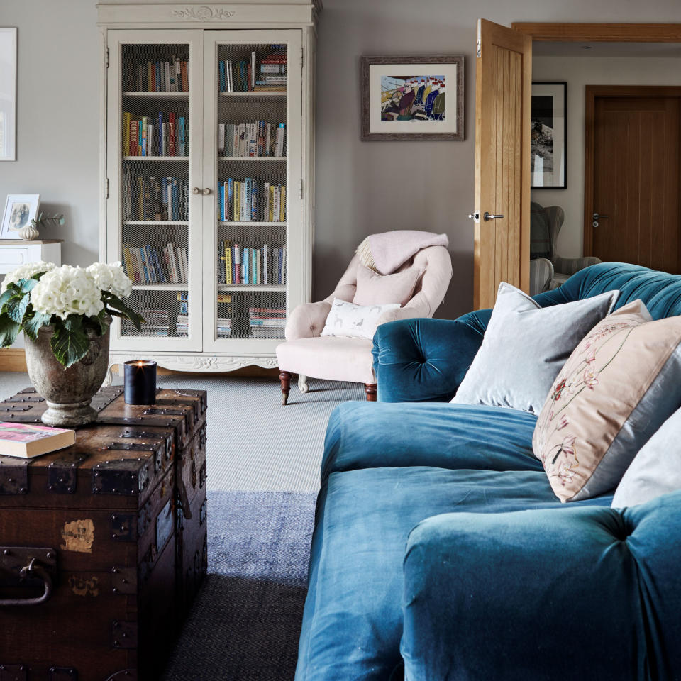 Blue velvet sofa in living room with scattered cushions displayed on top, armchair, and coffee table