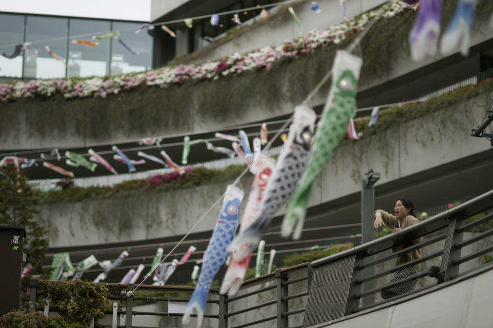 A woman sings a song near carp-shaped windsocks, or "koinobori," at the Skytree tower in Tokyo, April 30, 2024. Koinobori were installed to mark Children's Day celebrated on May 5. (AP Photo/Hiro Komae)