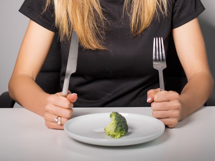 a woman looking down at a single piece of broccoli on a plate, under-eating