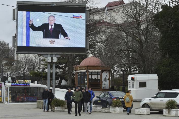 People walk in front of a TV screen in Sevastopol, Crimea, showing Putin during his state of the nation address.