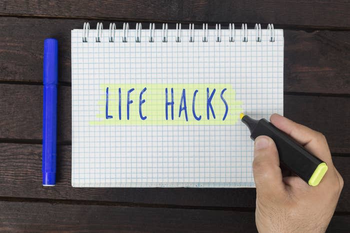 A hand highlights "LIFE HACKS" written on a spiral notepad with a blue marker, emphasizing self-improvement tips