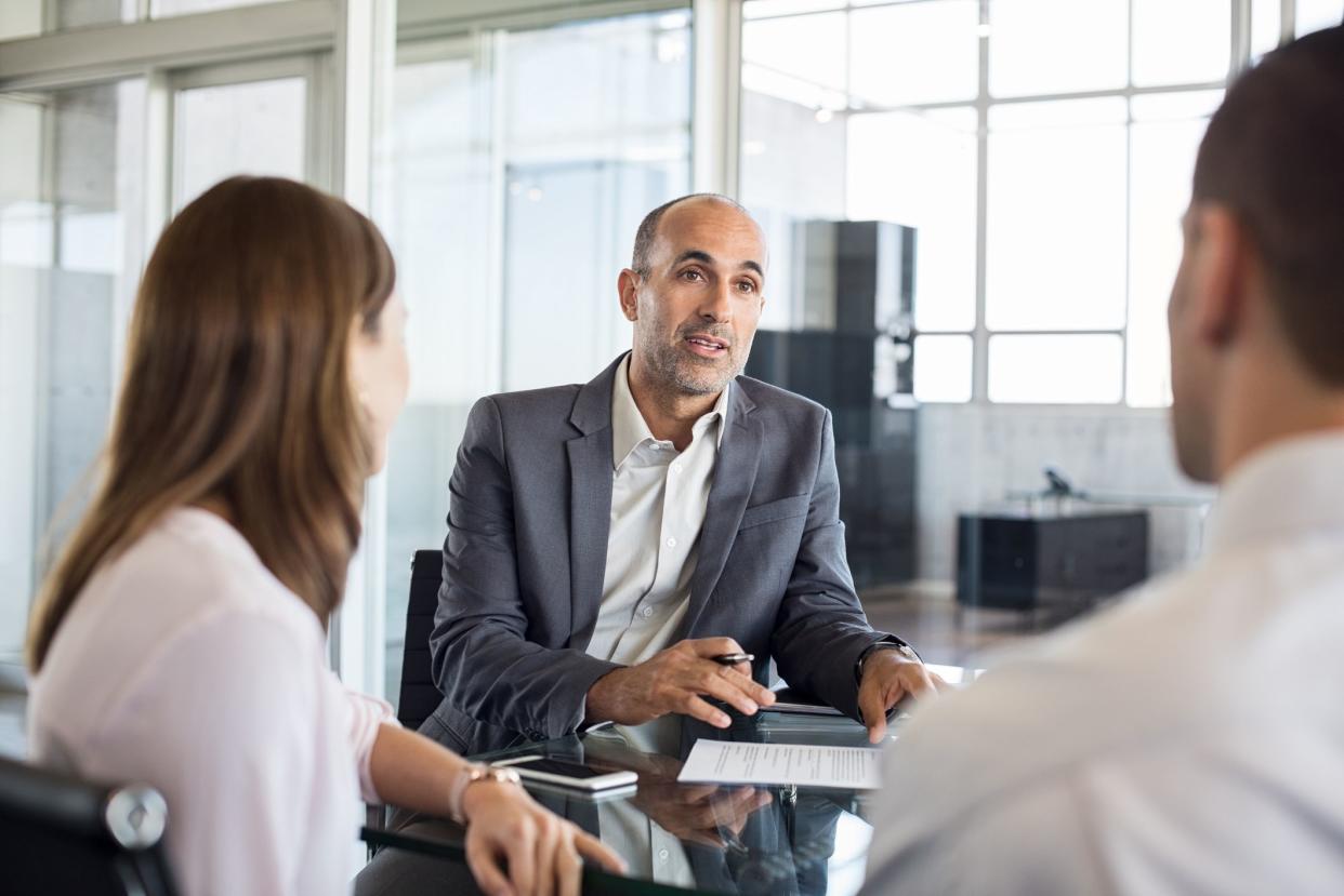 Mature financial agent showing new investment to young couple. Happy financial advisor discussing with a couple their mortgage loan. Happy couple consulting their bank agent about savings plan.