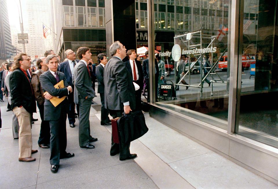 Somber-faced men stand outside the New York offices of a major mutual fund group watching an electronic display inside report the precipitous fall in the stock market, Oct. 19, 1987, in New York. In record heavy trading, all major stock indices were down heavily, with the Dow Jones Industrials off more than 300 points late in the day. 