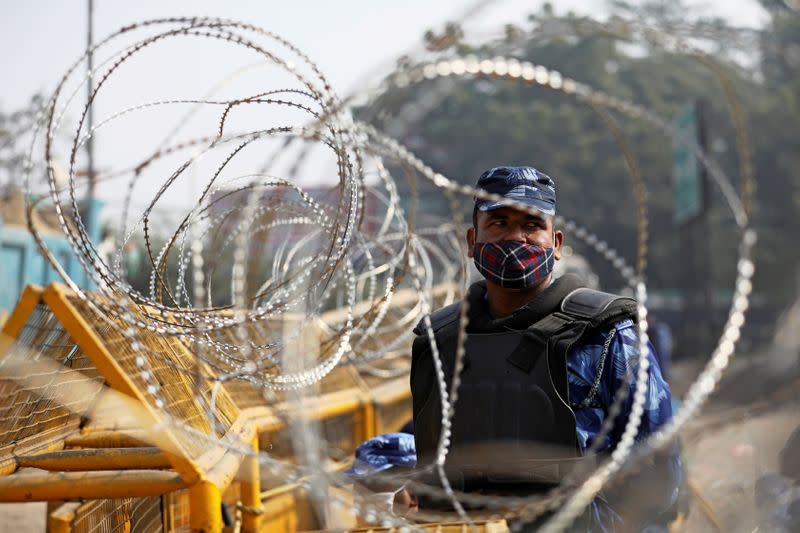 A member of the Rapid Action Force (RAF), wearing a protective face mask, is seen through barbed wire at the site of a protest against the newly passed farm bills at Singhu border near Delhi