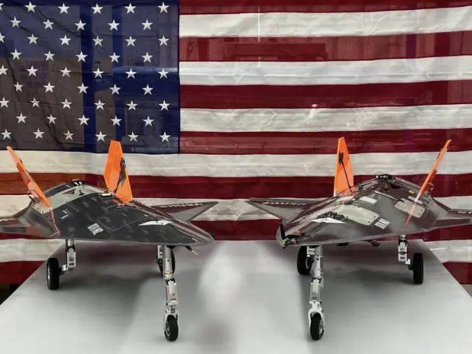 Two silver-coloured aircraft side-by-side in front of an American flag