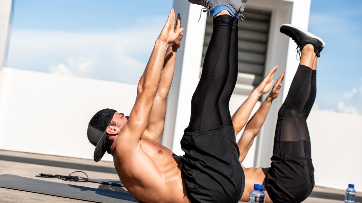  Group of athletic men doing toe touch crunch workout exercise outdoors on building rooftop floor 