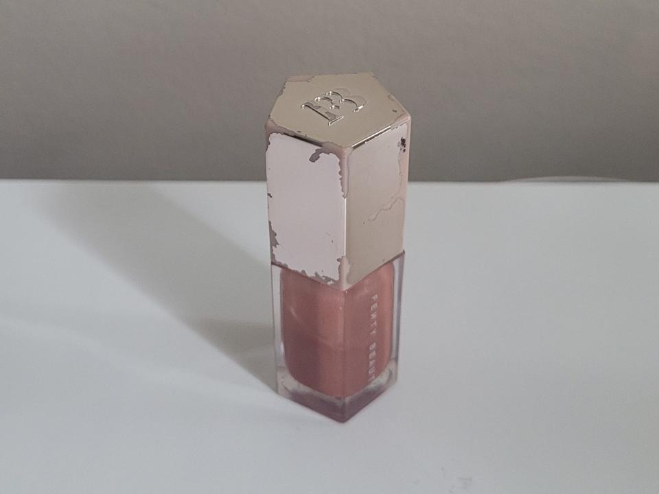 A Fenty Beauty gloss bomb lip product sits on a white table