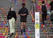 Spectators wearing masks walk past a hand sanitizer dispenser at court ahead of the first round matches at the Australian Open tennis championship in Melbourne, Australia, Monday, Feb. 8, 2021.(AP Photo/Hamish Blair)