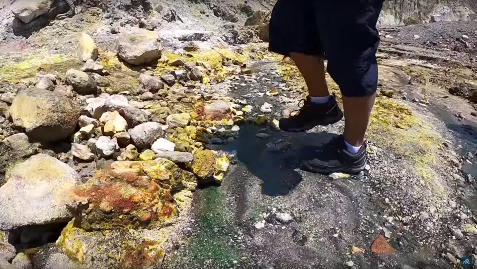 A man is seen walking near coloured rocks and water on White Island, New Zealand.