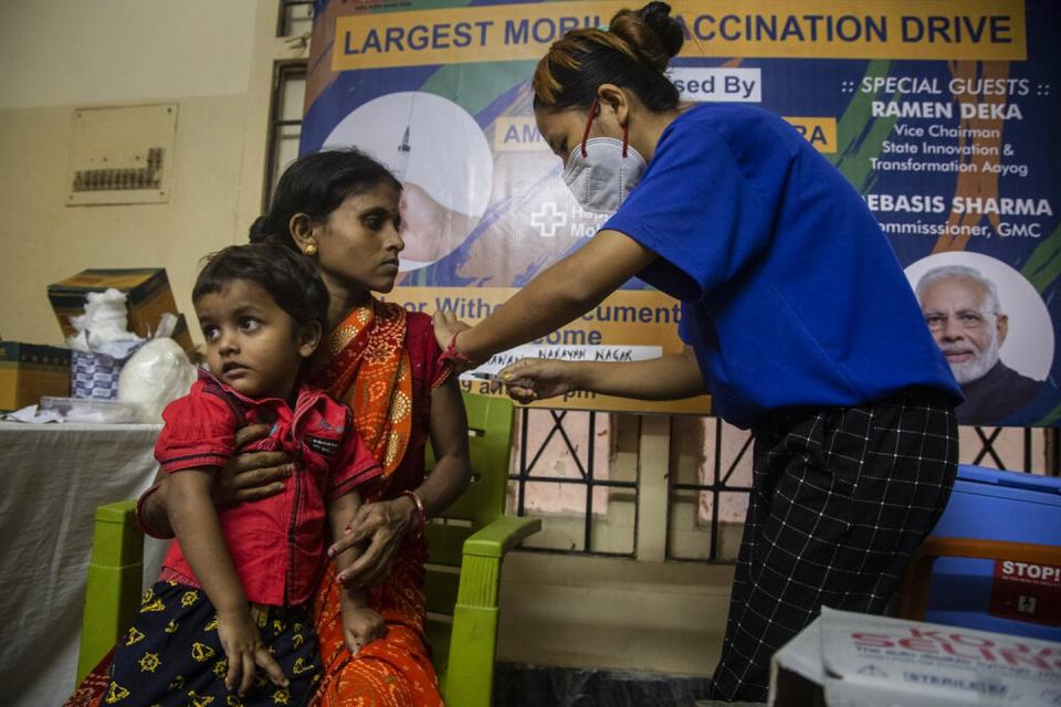 Woman holding child gets vaccinated by a health care worker in India.