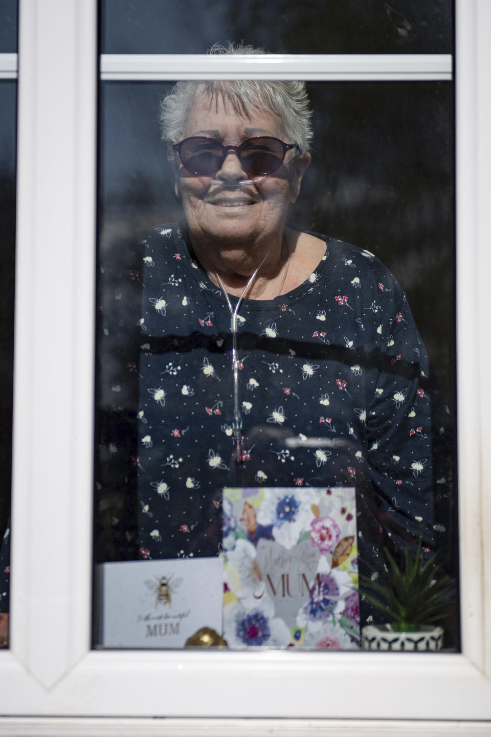 76-year old Olive Trotman, looks out from her home during as she is visited on Mother's Day by her son Mark, his wife Denise and his sister Kelly, in Napton, England, Sunday March 22, 2020. Olive suffers from a pulmonary disease and is taking the precaution of communicating at a safe distance or through a glass window, to limit the potential spread of COVID-19 coronavirus. Sunday is Mother’s Day in Britain and the government has a stark message for millions of citizens, that visiting your mom could kill her as for older adults and people with existing health problems, the virus can cause severe illness, including pneumonia. (Jacob King / PA via AP)