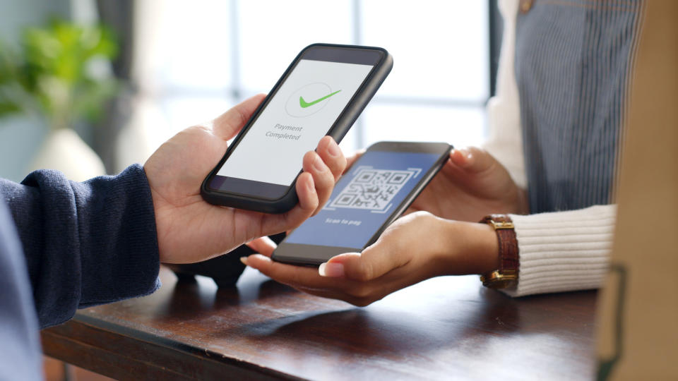 One person holds a phone displaying "Payment Completed," while another person holds a phone showing a QR code