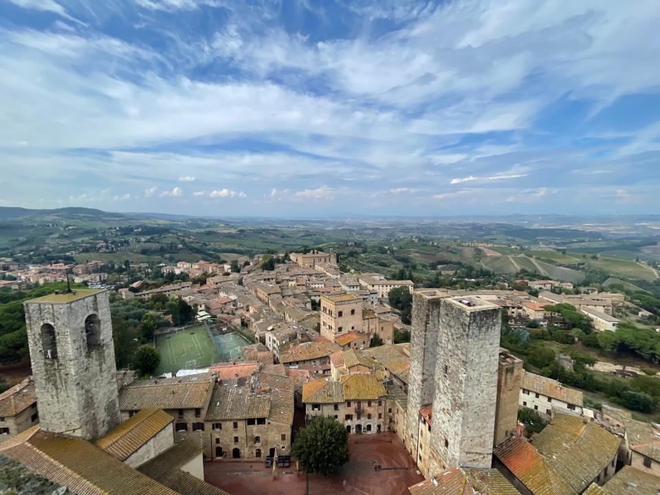 Vast blue skies with rolling fields and brown and gray Italian buildings in foreground in San Gimignano