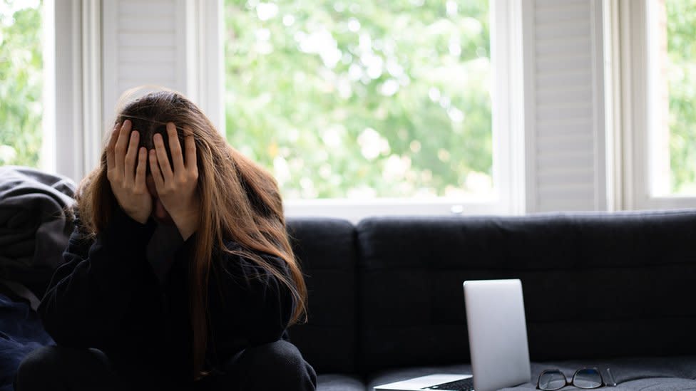 Una mujer apoyando la cabeza en las manos al lado de una computadora.