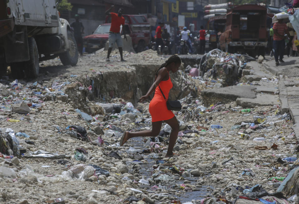 A woman crosses a storm drain filled with trash in Port-au-Prince, Haiti, Monday, May 27, 2024. (AP Photo/Odelyn Joseph)