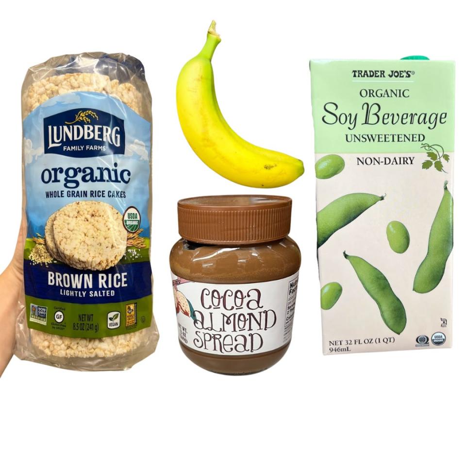 The writer holds a package of rice cakes next to a banana, a jar of cocoa-almond spread, and a carton with soybeans on it