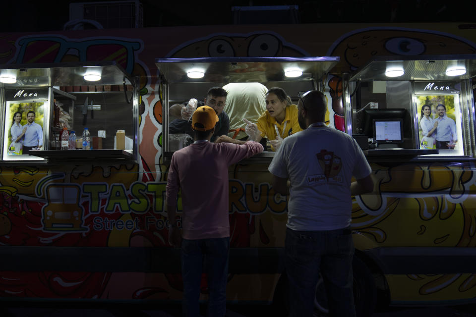 Jordanians buy sandwiches from a street vendor with posters of Jordan's Crown Prince Hussein and his fiancee, Saudi architect Rajwa Alseif decorating the van, during a concert at a sports stadium in Amman, Jordan, Monday, May 29, 2023. The free concert featuring well-known Arab singers, including Egyptian star Tamer Hosny, was part the celebrations leading up to the couple's wedding later this week. (AP Photo/Nasser Nasser)