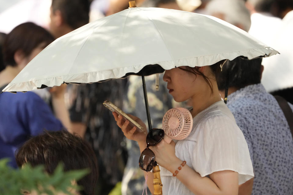 A woman uses a parasol and portable fan to protect from the sun at Ginza district in Tokyo, Japan, Friday, Aug. 4, 2023. Hot weather continues in the metro area as temperatures rise higher than 36 degrees Celsius (96.8 degrees Fahrenheit), according to Japan's meteorological bureau. (AP Photo/Shuji Kajiyama)