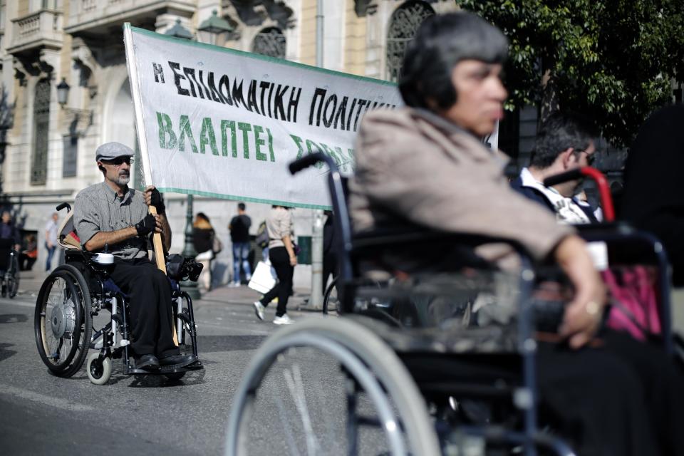 FILE - In this Thursday, Oct. 31, 2013 file photo, a man in a wheelchair holding a banner which reads in Greek "State benefit policy harms our health" takes part in an anti-austerity demonstration in central Athens. Researchers have found new evidence that Greece’s financial crisis is taking a toll on the health of its citizens, including rising rates of HIV, tuberculosis, suicides and even infant deaths. Since the economic crisis first hit several years ago, the government’s health spending has been slashed and hundreds of thousands of people have been left without health insurance. As cuts have been made to AIDS prevention programs, rates of HIV and tuberculosis in drug users have spiked. (AP Photo/Petros Giannakouris, File)