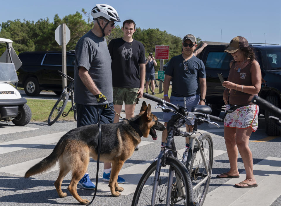 President Joe Biden stands with his dog Commander as he talks with a woman at Gordons Pond in Rehoboth Beach, Del., Saturday, June 18, 2022. Earlier Biden fell as he tried get off his bike to greet a crowd along the trail. (AP Photo/Manuel Balce Ceneta)