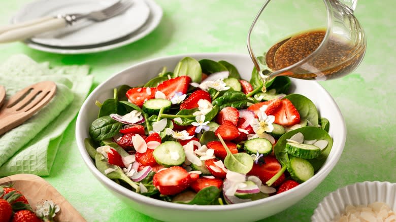 Pouring balsamic dressing into a strawberry spinach salad