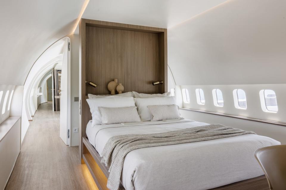A bedroom sits inside of a plane. The bed has a built-in, wooden headboard.