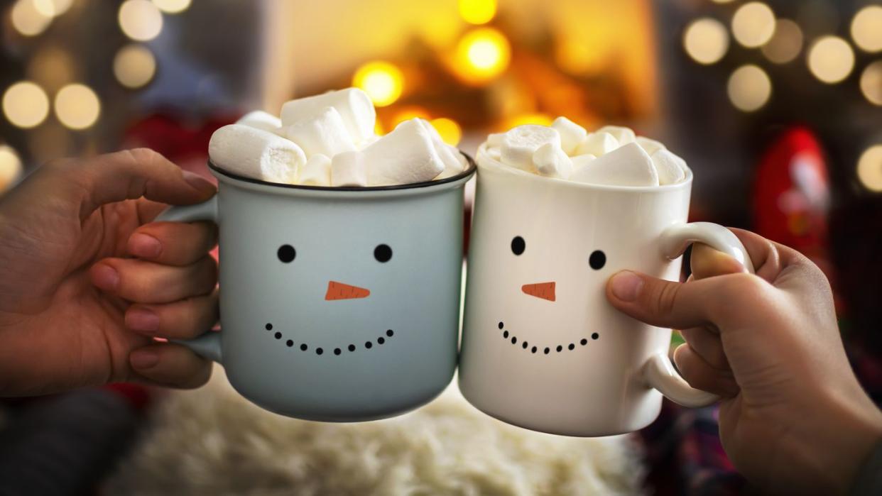 mom and child are relaxing together on a cozy winter evening by the fireplace, close up of two hands with snowman face cup of hot cocoa with marshmallows christmas holidays, happy moments at home