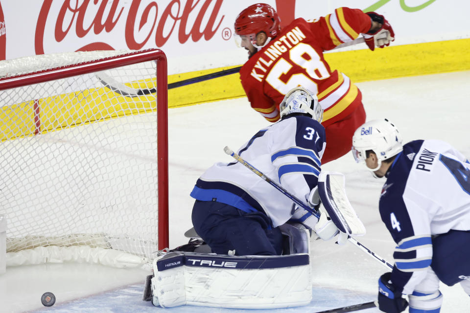 Winnipeg Jets goalie Connor Hellebuyck is scored on by Calgary Flames' Oliver Kylington (58) during the first period of an NHL hockey game in Calgary, Alberta, Monday, Feb. 19, 2024. (Larry MacDougal/The Canadian Press via AP)