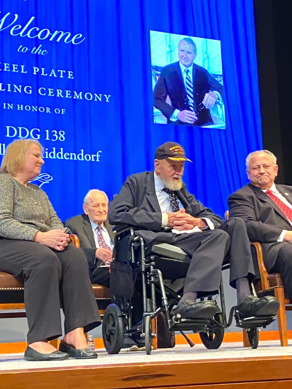 Little Compton resident J. William Middendorf, center, is flanked by Jill Boward, director for Combatant Ships at the Department of the Navy, and Navy Secretary Carlos Del Toro at a Naval War College ceremony to unveil the keel plate for the new destroyer that will be named after Middendorf, a former Navy secretary and diplomat. Author Ken Dooley is seated behind them.