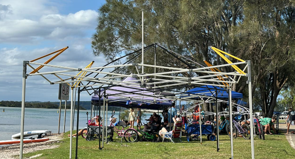 Australia Day revellers sit on camp chairs under gazebos by the beach, with many gazebos in various stages of construction at Swansea Bay beach.. 