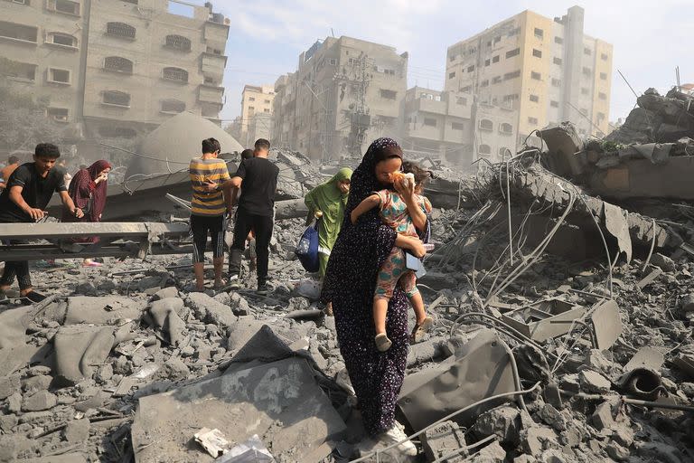 Una mujer palestina camina con su hijo en brazos entre los escombros