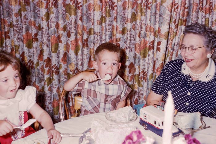 Two children and a grandmother at a birthday party with a cake on the table