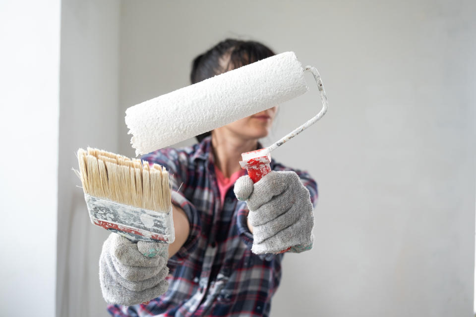 puzzled woman in paint roller and white paint for walls in hands close-up portrait. Construction work and cosmetic repairs in house, wall painting, tinting, finishing work with your own hands