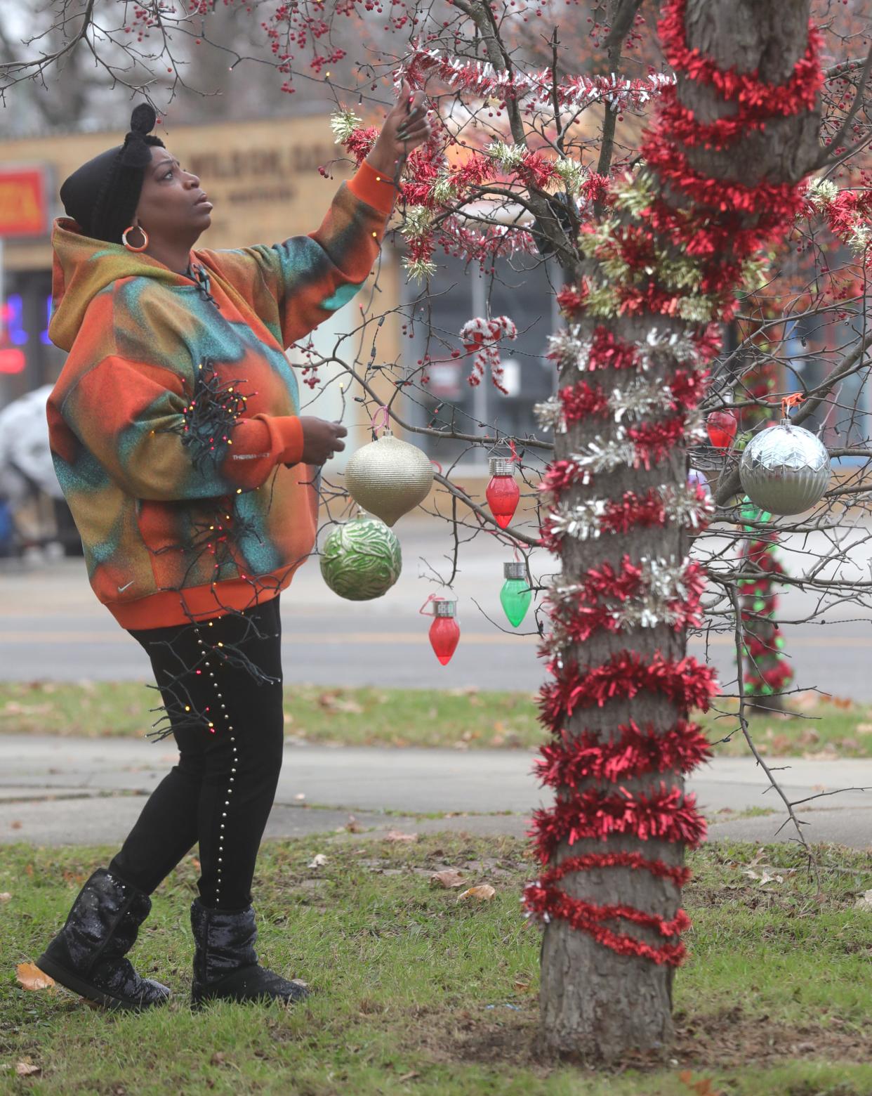 Fannette Morris, president of the Maple Valley Merchants Business Association, strings lights Monday on a tree at the corner of Nome Avenue and Copley Road in Akron