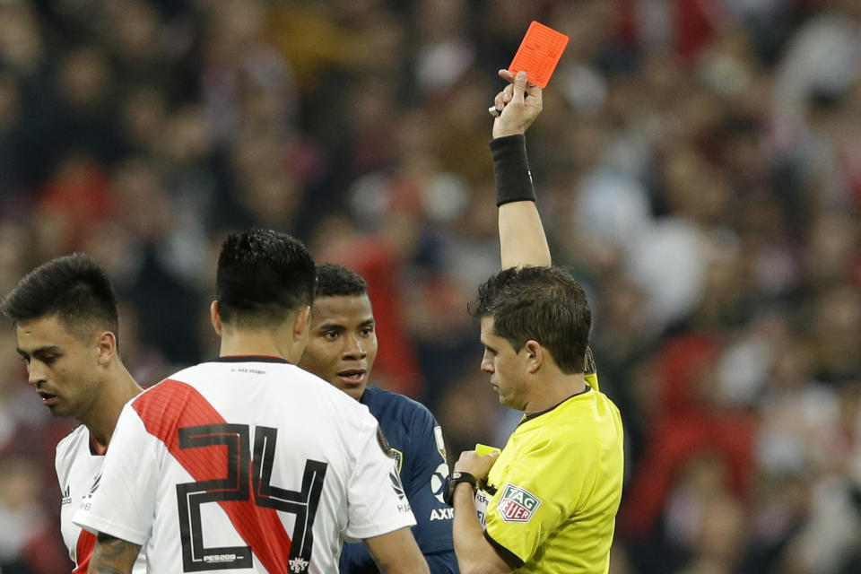 Referee Andres Cunha, of Uruguay, shows a red card to Wilmar Barrios of Argentina's Boca Juniors, center in blue, during a Copa Libertadores final soccer match between River Plate and Boca Juniors at the Santiago Bernabeu stadium in Madrid, Spain, Sunday, Dec. 9, 2018. (AP Photo/Armando Franca)