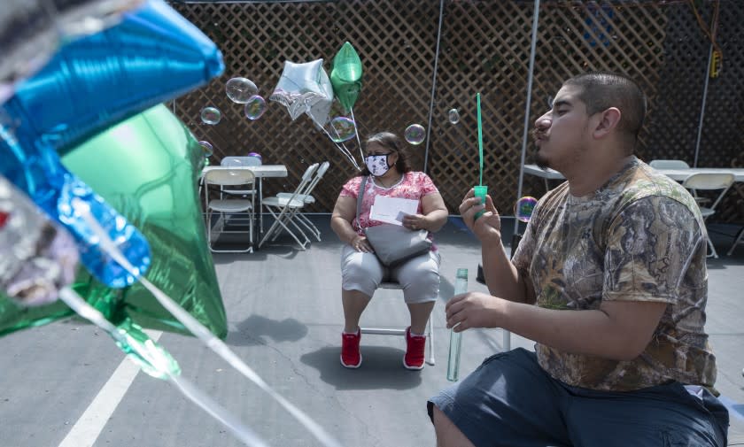 REDONDO BEACH, CA - APRIL 11: Daniel Arana, 20, blows soap bubbles in the post-shot waiting area with his mother Yolanda following his mock vaccination on Sunday, April 11, 2021 at Friendship Foundation in Redondo Beach, CA. The mock clinic is being held at the Friendship Foundation through Disability Voices United in Redondo Beach for individuals with intellectual disabilities. Real nurses will use syringes without the needle in an environment meant to mimic a vaccine site to help prepare vulnerable people for the vaccine, which they'll get in a few weeks. The event will be used to train Curative staff. (Myung J. Chun / Los Angeles Times)