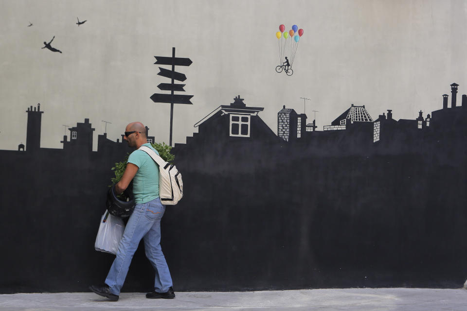 A cafe-bar owner prepares to place potted plants in front of a cityscape mural at his shop in Athens, on Friday, Sept. 6, 2013. (AP Photo/Petros Giannakouris)