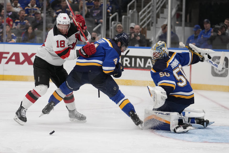 New Jersey Devils' Ondrej Palat (18) reaches for a loose puck as St. Louis Blues goaltender Jordan Binnington (50) and Nick Leddy (4) defend during the third period of an NHL hockey game Friday, Nov. 3, 2023, in St. Louis. (AP Photo/Jeff Roberson)