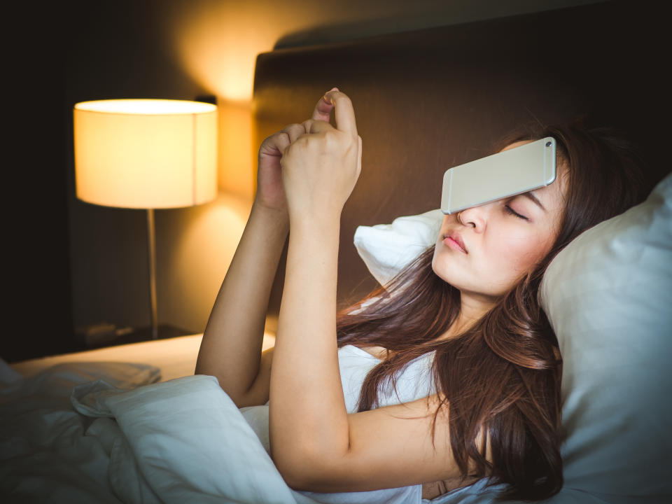 Sleepy asian woman in white bed, dropped smart phone on face