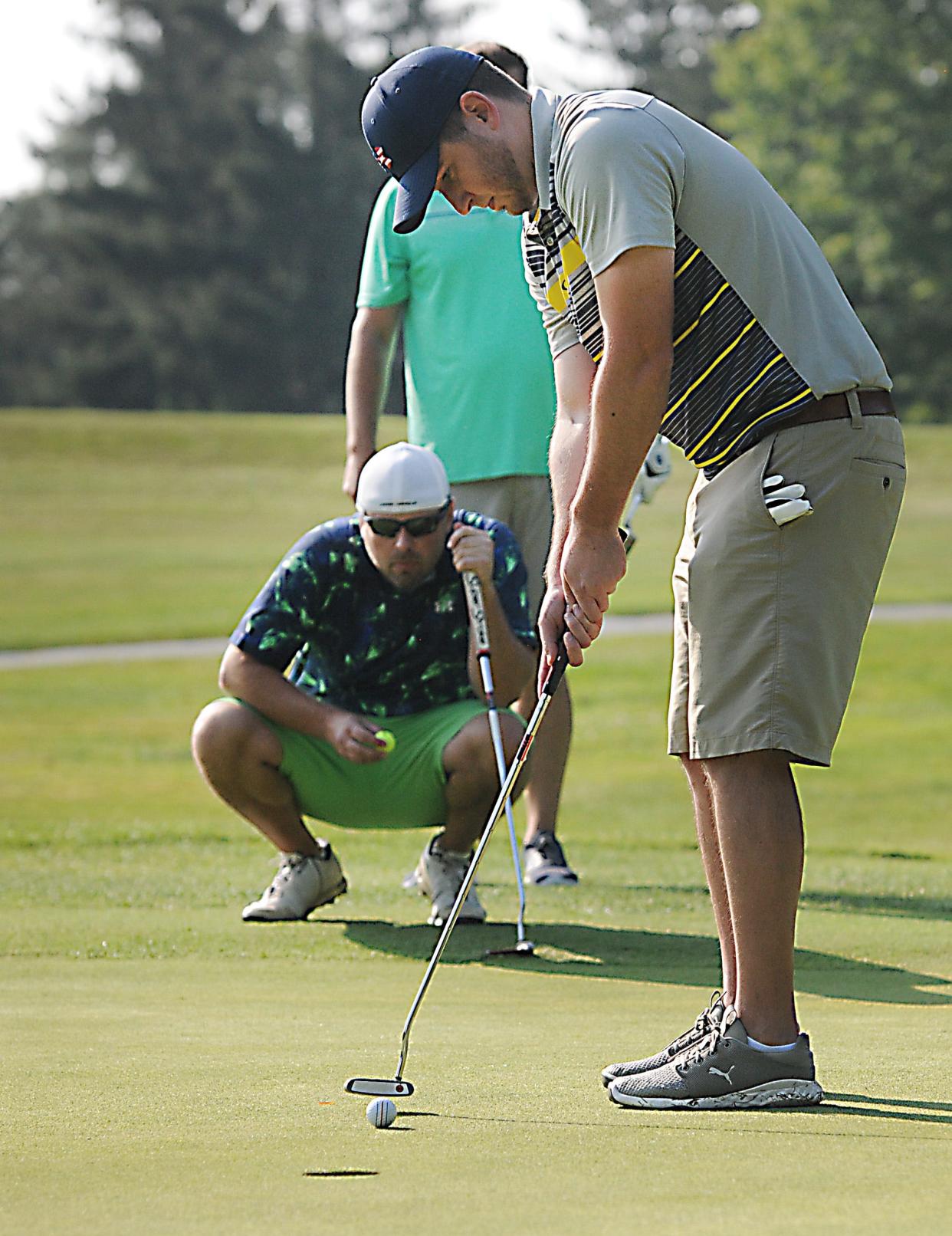 Rob Kocher putts as teammate R.J. Kocher, squatting in back, looks on Aug. 6, 2021, during the 26th Greater Alliance Carnation Festival Golf Scramble at Tannenhauf Golf Club. The 2023 event will be held Aug. 4 at Tannenhauf.
