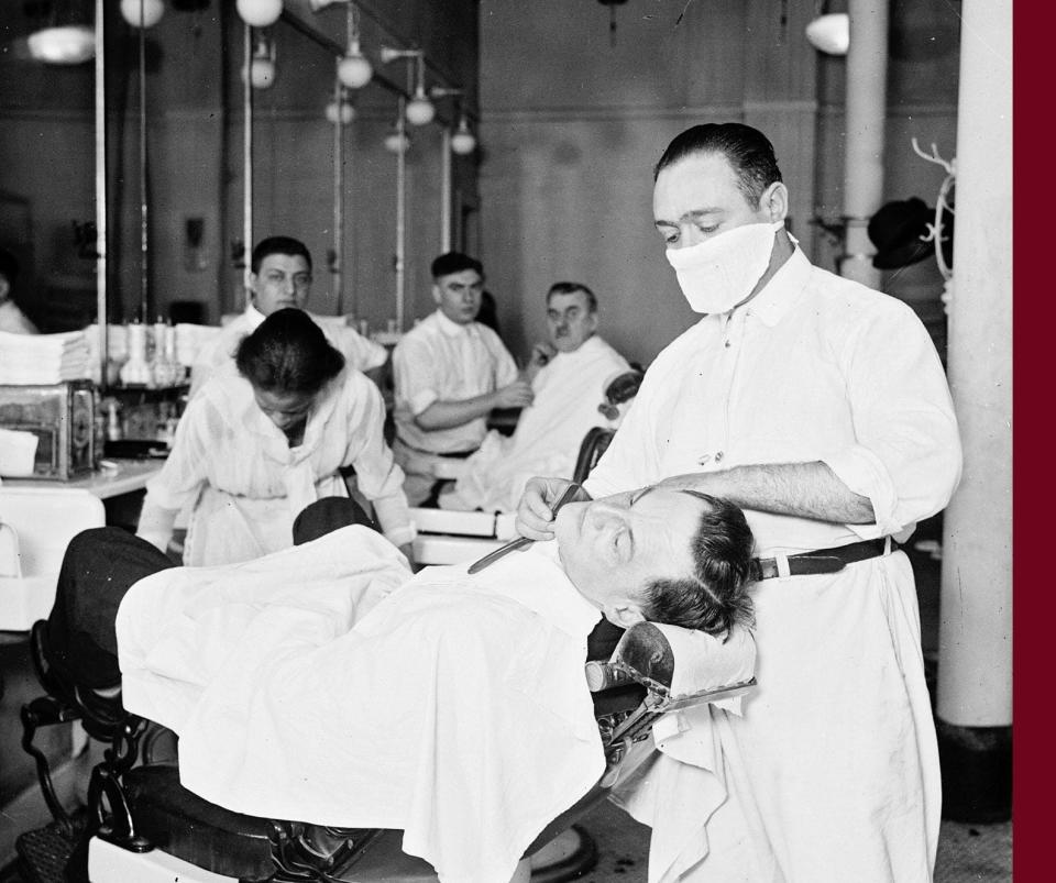 A barber in a barbershop shaving a man's face wears a mask to protect against influenza in Chicago in 1918.